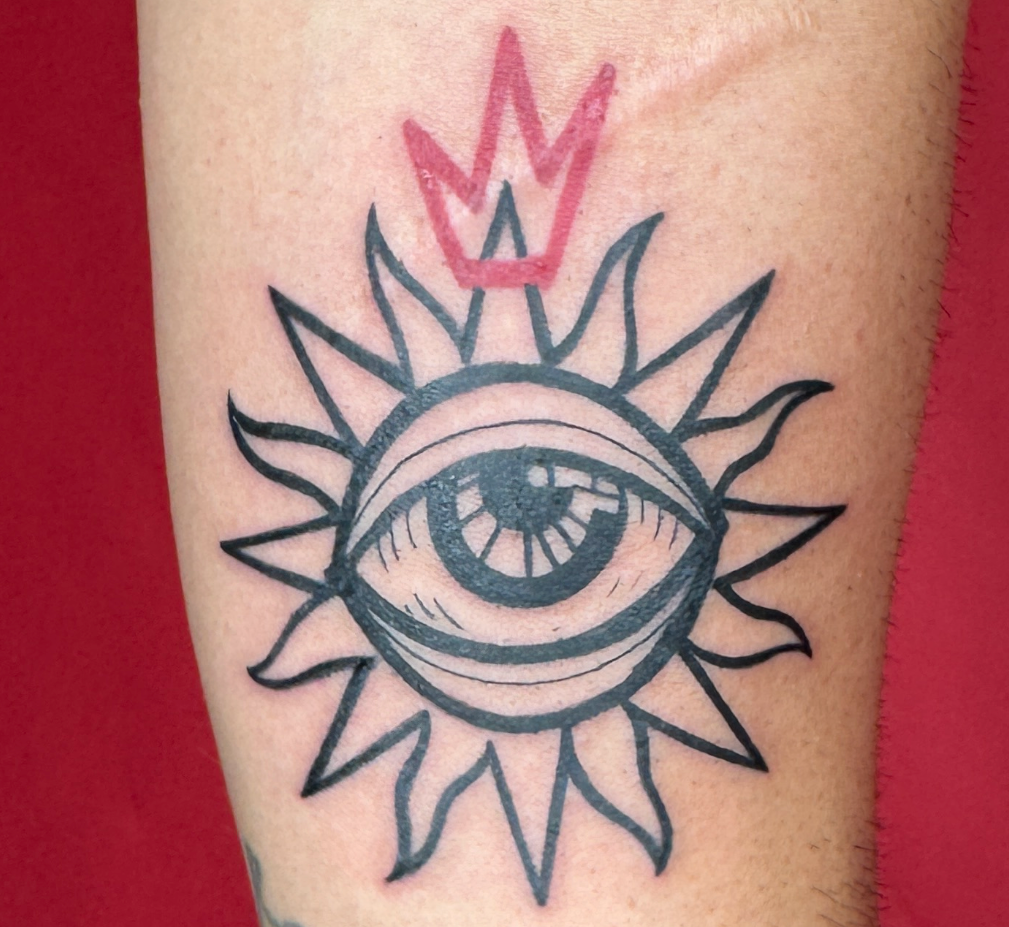 Tattoo of a sun - eye design on a person's arm against a red background